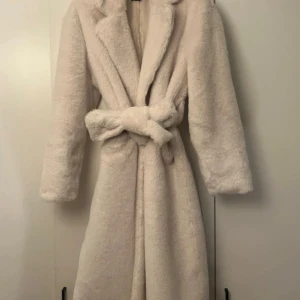PLT lång fuskpälskappa med midjebälte - Ej kommit till användning, nypris 799kr. Går ner till vaderna på mig som är 165cm :) fråga gärna om du undrar något!