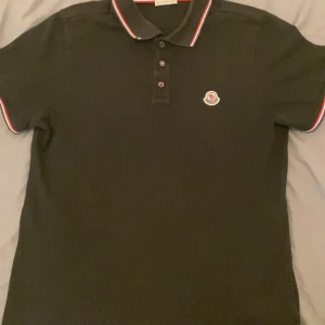 Moncler piké - Svart pikétröja från Moncler med klassisk krage och knappar framtill. Sitter bra och väldig stilig.