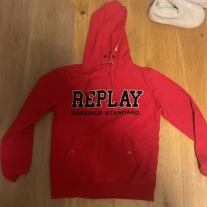 Sellsynt Röd hoodie från Replay med tryck - Riktigt snygg röd hoodie från Replay med stort REPLAY-tryck på bröstet och texten EIGHTYONE på huvan. Klassisk känguruficka med knappar och justerbar snörning i huvan. Perfekt för dig som gillar streetstyle och vill sticka ut.