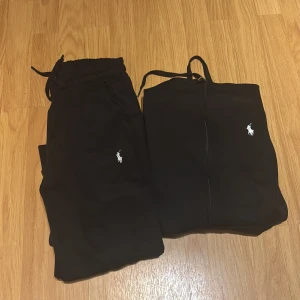Svarta tracksuit från Ralph Lauren - Svart tracksuit från Ralph Lauren med klassisk vit broderad logga på benet. Byxorna har resår och snörning i midjan för skön passform och är tillverkade i mjukt bomullsmaterial. Perfekta för chill eller träning.