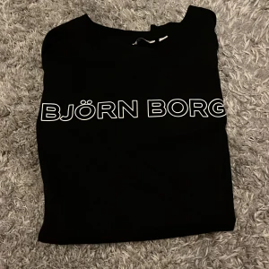 Svart Björn Borg t-shirt i bomull - Svart t-shirt från Björn Borg med vit logga tryckt över bröstet. Klassisk passform och rund halsringning. Tillverkad i mjuk bomull, perfekt för en clean och sportig look.
