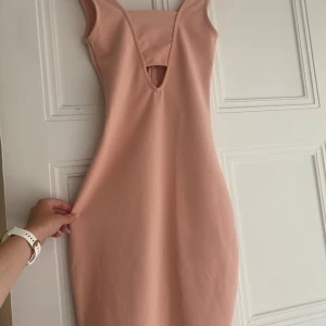 Ljusrosa tight klänning från Bik Bok - Supersnygg ljusrosa klänning från Bik Bok i tight passform. Modellen är ärmlös med v-ringning och en liten cut-out framtill. Klänningen är kort och har dragkedja i ryggen. Materialet är stretchigt i polyester och elastan, perfekt för dig som gillar en figurnära look.