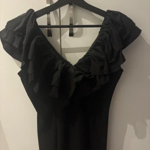 Svart volangklänning från Bubbleroom - Supersnygg svart klänning från Bubbleroom med bred volang runt v-ringningen och baktill🖤använd fåtal gånger så väldigt fint skick! Sitter tajt till kroppen, med dragkedja bak vid ryggen