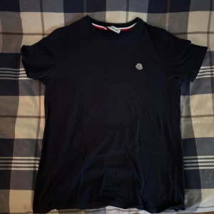 Moncler t-shirt - Snygg mörkblå t-shirt från Moncler med klassisk rund hals och liten broderad logga på bröstet. Tillverkad i mjuk bomull och har en enkel, stilren design. Perfekt för dig som gillar exklusiva basplagg med diskreta detaljer.