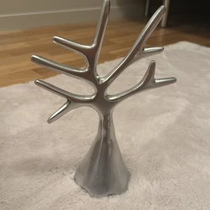 Smyckesträd i silverfärgad metall - Stilrent smyckesträd i silverfärgad metall med grenar för att hänga ringar, armband och halsband. Perfekt för att organisera dina favoritsmycken på ett snyggt sätt i rummet.