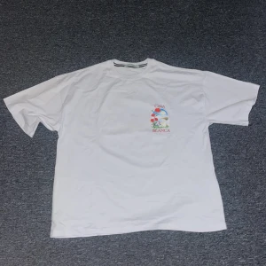 Vit Casa Blanca t-shirt med tryck - Vit t-shirt från Casa Blanca med färgglatt blommigt tryck och text på både bröstet och ryggen. Klassisk passform med rund hals och korta ärmar. Perfekt för dig som gillar stilrena plagg med en twist.