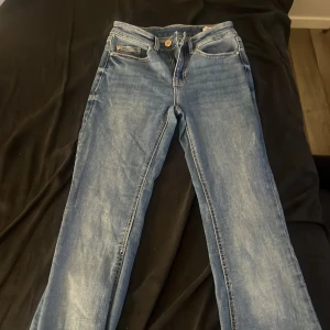 Blå raka jeans med klassisk look stl xs - Snygga blå utsvängda jeans med klassisk femficksdesign. Jeansen har normal midja, ljus tvätt och en läderpatch bak i midjan. Perfekta för dig som gillar en tidlös och avslappnad stil. Materialet är slitstarkt denim i bomull.