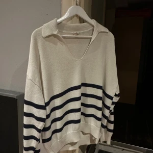 Randig stickad tröja med krage - Säljer en stickad tröja i beige med mörkblå ränder. Tröjan har en avslappnad passform, v-ringning