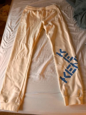 Kenzo mjukis byxor - Säljer ett par Mjukis byxor från märket kenzo, Dem är beigea med blå text, Dem är nästintill nya, dem är inte använda en enda gång utan köpte för 2 år sedan, Dem är köpta på Nk i Göteborg och har bara legat i en låda sedan dess