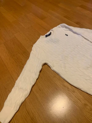 Vit kabelstickad tröja Polo Ralph Lauren - Vit kabelstickad tröja från Polo Ralph Lauren i storlek M. Klassisk design med rund hals och svart broderad logga på bröstet. Tröjan har långa ärmar och ribbade muddar vid hals, ärmslut och nederkant. Perfekt för dig som gillar preppy stil. Passar S mer än M men hade kunnat passa m oxå  Taggar finns fortfarande på , men ja glömde ta en bild på dom skriv för fler bilder 