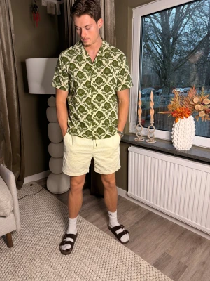 Grön blommig kortärmad skjorta från LES DEUX - Säljer en kortärmad skjorta med grönt blommigt mönster på vit botten från LEX DEUX . Skjortan har klassisk krage och rak passform, perfekt för dig som gillar att sticka ut med coola prints. Materialet känns lätt och luftigt, perfekt för varmare dagar.