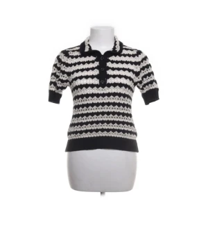 Randig stickad pikétröja från MNG - Snygg stickad pikétröja från MNG i svart och vitt med korta ärmar och krage. Tröjan har ett randigt mönster, knappar framtill och är gjord i ett mjukt stickat material. Perfekt för dig som gillar retrovibbar och vill sticka ut lite extra.