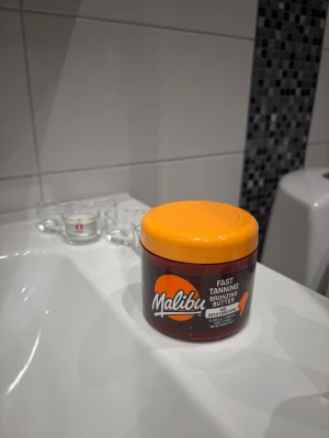 Malibu Fast Tanning Bronzing Butter - Malibu Fast Tanning Bronzing Butter med betakaroten i en rund burk med orange lock. Smöret är intensivt gult och har en krämig konsistens. Perfekt för att få en solkysst glow snabbt. Innehåller 300 ml och är vattenresistent. Ni ser på bild 2 vad som är använt. Endast testad 