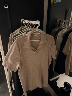 Beige piké från  ” East west ” ( HELT NY ) - Snygg beige skjorta från Selected Homme med korta ärmar och klassisk krage, perfekt för en chill och stilren look. Tröjan är helt ny och aldrig använd!