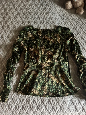 Blommig långärmad blus från Vero Moda - Säljer en snygg blommig blus från Vero Moda i storlek M. Blusen har svart botten med gröna och beige blommor, långärmad och lätt puff vid axlarna.  Tröjan har knappt använts så den är i fint skick