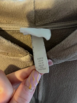 Beige fleece hoodie med dragkedja  - Mjuk och skön beige hoodie i fleece med dragkedja framtill och två stora fickor. Tröjan har huva och långa ärmar, perfekt för chill dagar. Croppad passform som ger en avslappnad vibe. Snygg att matcha med jeans eller mjukisbyxor.