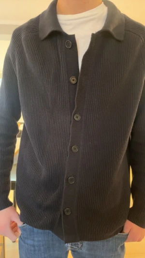 Marinblå kofta från John Henric - Snygg marinblå kofta från John Henric i ribbstickad bomull. Koftan har klassisk krage, knäppning med fem knappar och långärmad design. Perfekt att slänga över en t-shirt för en chill och stilren look. Passar dig som gillar enkel och tidlös stil.