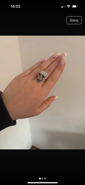 En coola silverringar med detaljer - Säljer två unika ringar i silverfärg. Den ena är en chunky ring med döskalle och glittrande stenar, perfekt för dig som gillar edgy stil. Den andra är en stilren och enkel ring med en snygg böjd design. Båda passar dig som vill sticka ut med dina accessoarer.