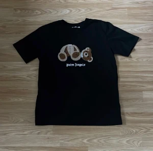 Svart Palm Angels t-shirt med björn - Svart t-shirt från Palm Angels med broderad björn på bröstet och vit Palm Angels-logga under. T-shirten är i 100% bomull och har en klassisk rund hals samt korta ärmar. Björnmotivet är i beige och bruna toner med tydlig struktur.