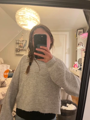 Grå stickad tröja från Kappahl - Mysig grå stickad tröja från Kappahl med krage och avslappnad passform. Tröjan är croppad med långa ärmar och ribbade muddar. Perfekt för lager-på-lager och chill dagar. Snygg till jeans eller kjol!