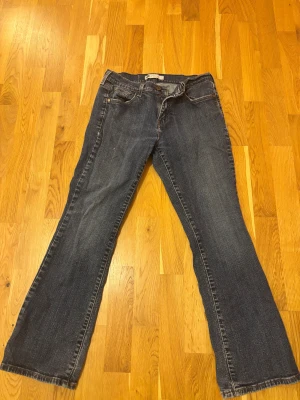 Levi's 505 mörkblå bootcut jeans - Snygga Levi's 505 jeans i mörkblå med klassisk bootcut passform. Jeansen har fem fickor, gul kontrastsöm och det ikoniska röda Levi's-märket på bakfickan. Materialet är slitstarkt denim och midjan är normal. Perfekt för dig som gillar retrovibe och tidlös stil.