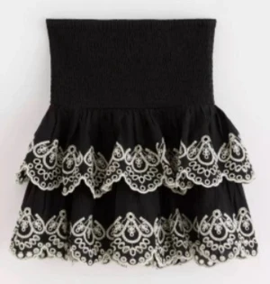 Svart volangkjol med broderi - Supersöt svart kortkjol med bred smock i midjan och två lager volanger. Använd fåtal gånger! 