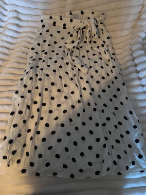 Prickig omlottkjol från & Other Stories - Supersöt vit omlottkjol från & Other Stories med svarta prickar och knyt i midjan. Kjolen har en luftig och flowy känsla, perfekt för dig som gillar en lekfull och trendig stil. Passar lika bra till sneakers som sandaler.