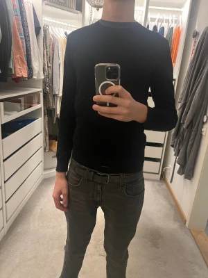 Svart stickad tröja - En svart långärmad tröja från WE i bomull, med rund hals och diskreta grå ränder vid kragen. Enkel och stilren modell som passar perfekt till jeans eller chinos. Tröjan har en normal passform och är riktigt skön att bära.