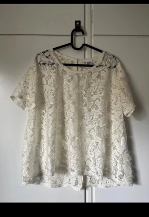 Vit spetsblus från Vero Moda - Säljer en vit blus från Vero Moda i genombruten spets med blommigt mönster. Blusen har rund halsringning och korta ärmar. Perfekt för dig som gillar romantisk och luftig stil.