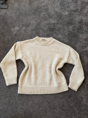 Beige stickad tröja - Snygg beige stickad tröja med rund hals och ribbade muddar vid ärmslut och nederkant. Perfekt för dig som gillar enkel och clean stil. Tröjan har långärmade ärmar och en loose passform som gör den skön att bära under kyliga dagar.