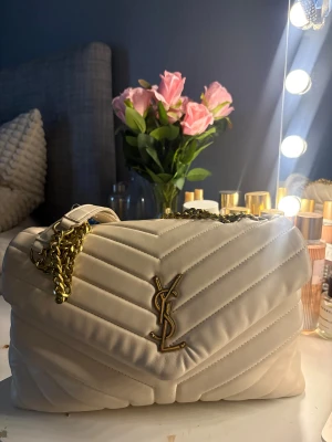 Vit quiltad axelväska från YSL - Säljer en snygg vit axelväska från YSL med några slitningar på bandet!! Skriv för mer bilder eller om du har frågor❤️Har tappar bort äktahetsbeviset i flytt därav priset!