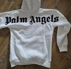 Vit hoodie med tryck - Säljer en vit hoodie med stor svart logga på ryggen och mindre logga framtill. Tröjan har huva med snörning, magficka och ribbade muddar. Perfekt för dig som gillar streetwear och vill sticka ut med en clean look.