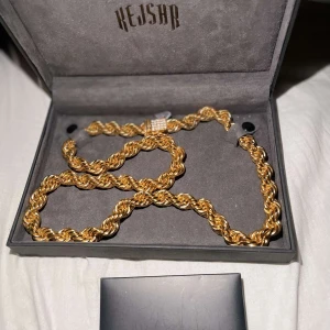 Guldigt halsband från Kejsar - Säljer ett fett halsband från Kejsar med tvinnad kedja i guldton och en blingad låsdel. Perfekt för dig som vill sticka ut med en riktigt snygg kedja. 65cm lång 10mm bredd guld platerat