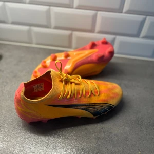 Gula och orangea Puma fotbollsskor - Säljer ett par snygga fotbollsskor från Puma i en riktigt fet färgkombo av gult och orange med svarta detaljer. Skorna har snörning och mönstrad sula med dobbar för gräsplan. Perfekta för dig som vill sticka ut på planen!