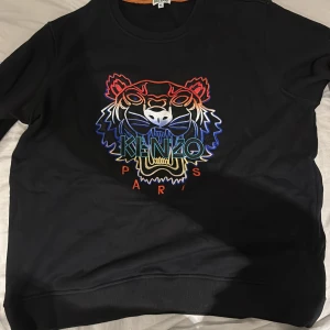 Svart Kenzo sweatshirt med tigerbrodyr - Svart sweatshirt från Kenzo med ikonisk broderad tiger i flera färger på bröstet och texten 'Kenzo Paris'. Tröjan är i 100% bomull, har rund hals och långa ärmar. Perfekt statement-plagg för dig som vill sticka ut med stil. Xl men passar M-L