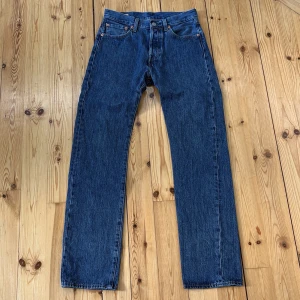 Levi's 501 blå jeans W28 L32 - Klassiska Levi's 501 jeans i blå denim med raka ben och normal passform. Byxorna har fem fickor, knappgylf och snygga kontrastsömmar. Märkta med Levi's Premium och har den ikoniska läderpatchen bak i midjan.