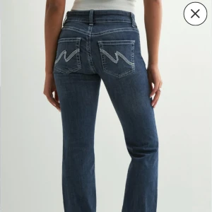Blå bootcut jeans från Nelly - Snygga blå jeans från Nelly med bootcut-modell och hög midja. Jeansen har dubbla knappar framtill och coola bakfickor med vit zigzag-detalj. Klassisk femficksdesign och stretchigt denimtyg som sitter skönt hela dagen.