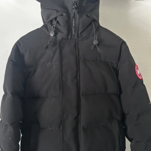 Canada Goose jacka  - Säljer en svart dunjacka från Canada Goose i storlek M. Jackan har huva, dragkedja framtill och klassisk Canada Goose-logga på ärmen. Självklart ingår original påse! NYPRIS:15000kr , MITT PRIS:2949