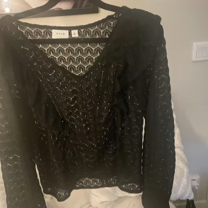 Svart spetsblus från Vila - Säljer en svart blus från Vila i storlek XS. Blusen är i genombruten spets med v-ringning och volangdetaljer framtill. Långärmad 