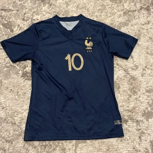 Frankrike Mbappé #10 fotbollströja - Snygg marinblå Frankrike fotbollströja size S från Nike med guldiga detaljer, nummer 10 och Mbappé på ryggen. Tröjan har korta ärmar, FFF-logga med tupp och två stjärnor på bröstet. Tillverkad i lätt och ventilerande material, perfekt för träning. Ni kan skriva pris hur mycket ni vill ha den för. Shorts ingår 
