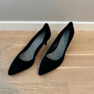 Svarta pumps från Filippa K, mocka - Stilrena svarta pumps från Filippa K i mjuk mocka med spetsig tå och klack. Klassisk och tidlös modell som passar perfekt till både jeans och klänning. Tillverkade i Portugal med äkta läder (vero cuoio) i sula. Snygg och elegant siluett.