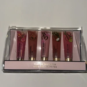 Victoria's Secret Flavor Favorites läppglans - Set med fem läppglans från Victoria's Secret i smakerna Pink Mimosa, Caramel Kiss, Candy Baby, Coconut Craze och Kiwi Blush. Tuberna är i olika nyanser av rosa och nude med guldiga detaljer och fruktmotiv på förpackningen. Perfekt för dig som gillar glossiga och smaksatta läppar.