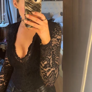 Svart spetsblus med djup v-ringning - Svart spetsbody med tight passform som går att klä både upp och ner