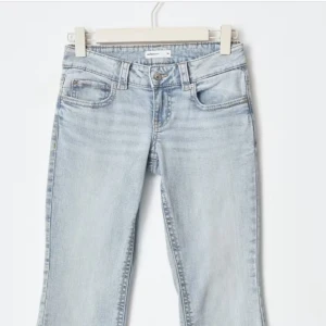 Ljusblå bootcut jeans med fickdetaljer - Snygga ljusblå jeans med bootcut passform och klassiska fem fickor, varav bakfickorna har lock och knapp. Jeansen har bälteshällor och är tillverkade i mjukt denimtyg. Perfekta för dig som gillar en avslappnad men trendig look.