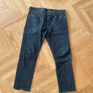Levi's 508 mörkblå jeans W34 L32 - Mörkblå Levi's 508 jeans med klassisk femficksdesign och råa, avklippta benslut. Jeansen har raka ben och tydliga kontrastsömmar. Tillverkade i slitstarkt denim med den ikoniska läderpatchen bak i midjan.