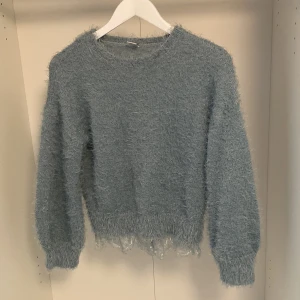 Ljusblå fluffig stickad tröja Lindex - Supermjuk och fluffig ljusblå stickad tröja från Lindex med långa ärmar och breda muddar. Nedtill finns en söt spetskant som ger extra detalj. Den har dessutom ballong ärmar. Perfekt för dig som gillar mysiga och unika plagg med lite extra stil. 