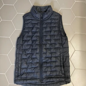 Svart dunväst från Everest - Snygg svart dunväst från Everest i storlek 146/152. Västen är quiltad med dragkedja framtill och har en hög krage. Tillverkad i syntetmaterial och perfekt för lager-på-lager under kyliga dagar. Enkel och stilren design som funkar till det mesta.