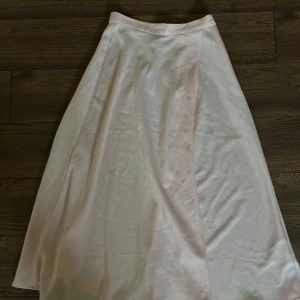 Ljusrosa långkjol i satin - En superfin ljusrosa långkjol i glansigt satinliknande material. Kjolen har en slitt och faller snyggt längs benen. Perfekt för dig som gillar en clean och stilren look med lite extra shine.