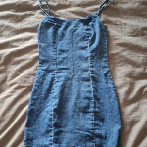 Blå jeansklänning från H&M Divided - Säljer en blå jeansklänning från H&M Divided i storlek 36. Klänningen är kort, har smala axelband och en figurnära passform. Dragkedja bak för enkel påklädning. 