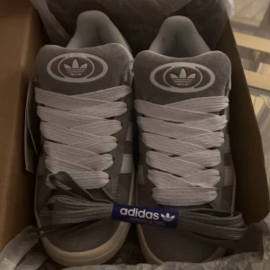 Adidas Campus grå sneakers mocka - Säljer mina Adidas sneakers i storlek 36 1/2.  Skorna är helt nya, aldrig använda och taggen sitter fortfarande kvar. Klassisk grå färg med vita detaljer och riktigt bekväma att ha på sig. Perfekta både till vardags och för en snygg streetstyle-look 👟✨. Kan mötas upp eller skicka 💕.